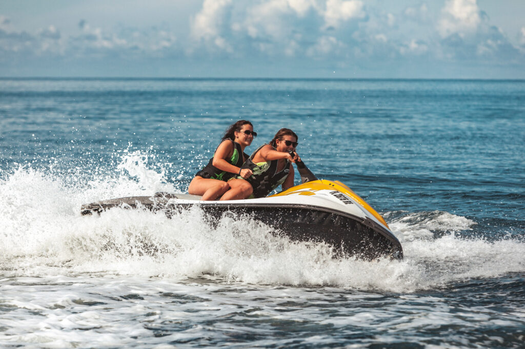 Two girls on a jet ski turning sharply and making waves
